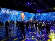 View of Exhibition Van Gogh: The Immersive Experience at AREA15. The room is filled with people in VR goggles, the lighting on the crowd has brought starry night into the room, details of stary night are projected on the walls. 