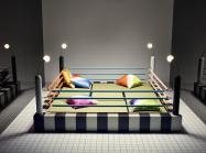 a bed or sitting area designed to resemble a boxing ring. With pillows in four corners and the ropes, lights and elevated platform of a ring.  