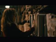 Lynda is seen in dark room, looking at shelf packed with documents. 