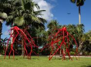 large red metal sculpture of roots in a garden