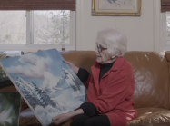 Woman holding bob ross painting on couch
