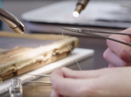 close up shot of hand with tweezers holding string for canvas weaving