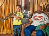boy playing trumpet, father sits beside him holding a black and white photo
