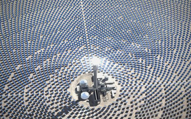 Seen from above, rings of mirrors spread across a desert around a glowing solar tower
