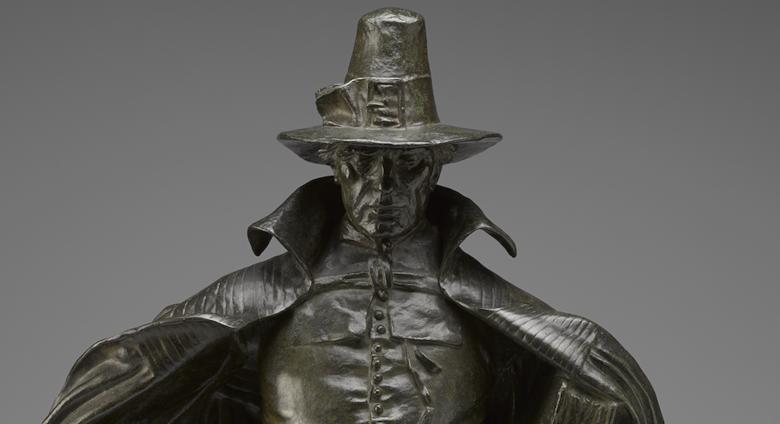 The figure looks directly at the viewer, with large hat and cape. The hat casts a shadow over part of the figure's face as detailed later. 