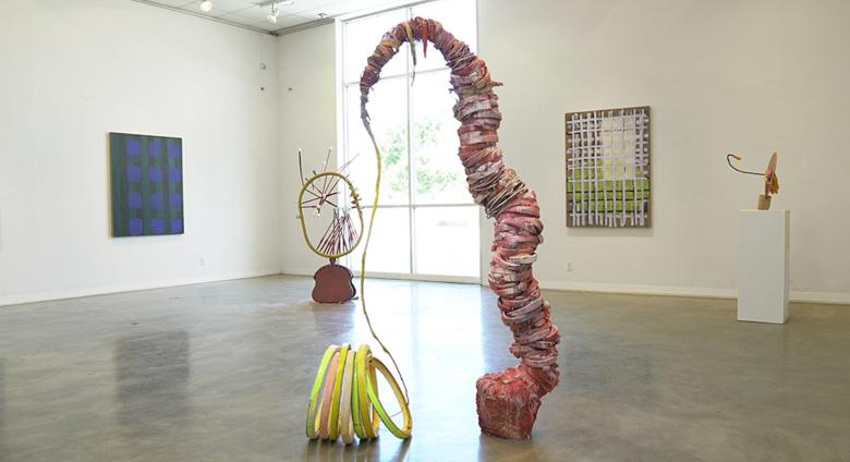 Installation view of Evenso: The Common & The Curious, showing sculpture in center of room and works on walls