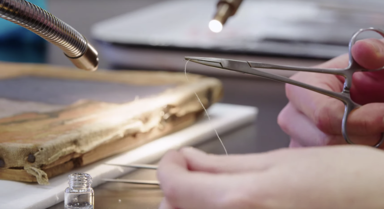close up shot of hand with tweezers holding string for canvas weaving