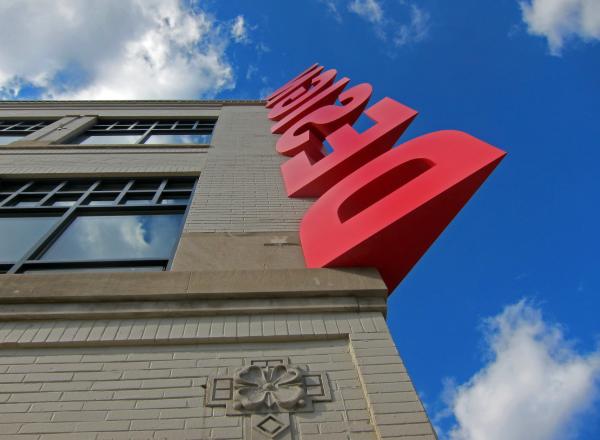 the word "design" in large red letters running up the corner of a building towards a bright blue sky