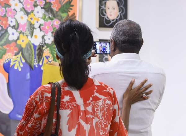 A couple at the Affordable Art Fair NYC, taking a photo of a bright, contemporary still life floral painting. 