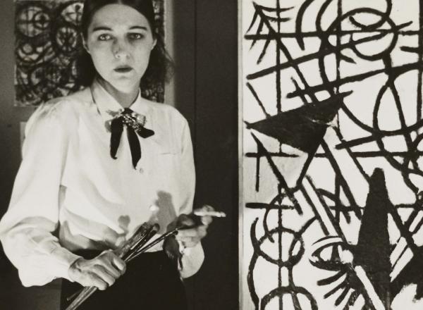 artist stands next to her work, brushes in hand but nicely dressed. Her features and clothes are as strikingly monochrome as her artwork. 