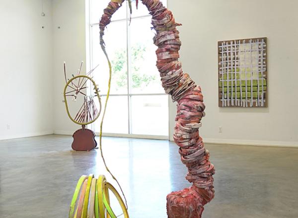 Installation view of Evenso: The Common & The Curious, showing sculpture in center of room and works on walls