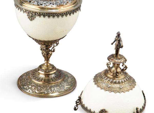the base and cover with chased strapwork and fruit, the cover surmounted by the figure of Judith holding the head of Holofernes, the interior with a hinged, pierced lid covering the bottom half of the cup, inset with a 1768 Nuremburg thaler.