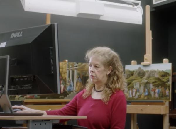 conservator looks at computer in front of several paintings