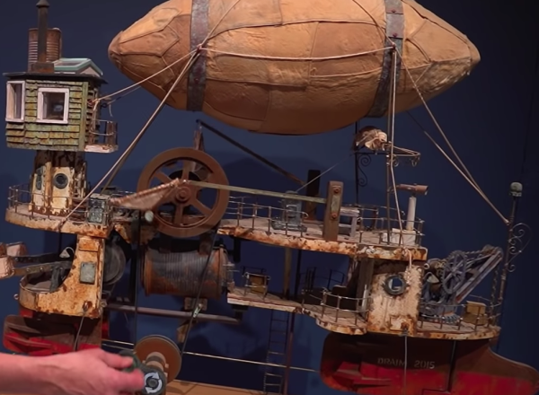 Woman turns handle of steampunk blimp ship sculpture