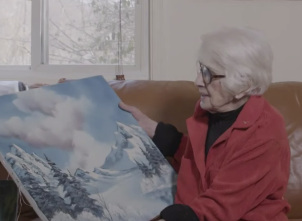 Woman holding bob ross painting on couch