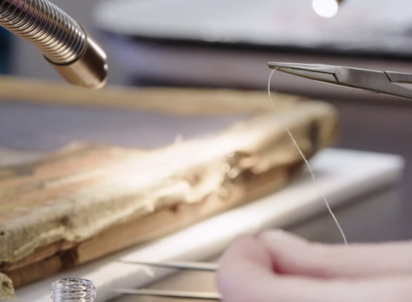 close up shot of hand with tweezers holding string for canvas weaving