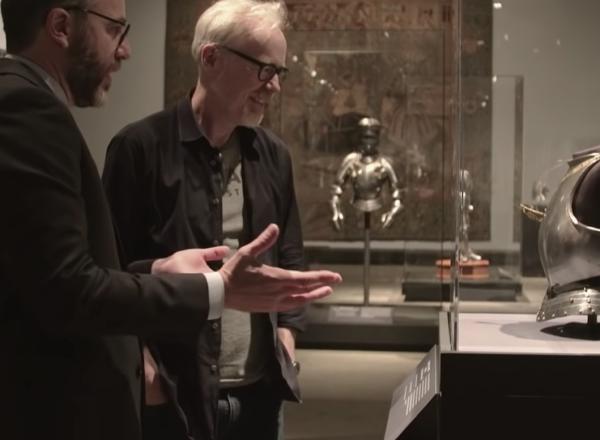 Adam Savage and Met Curator look at child's breastplate in glass case