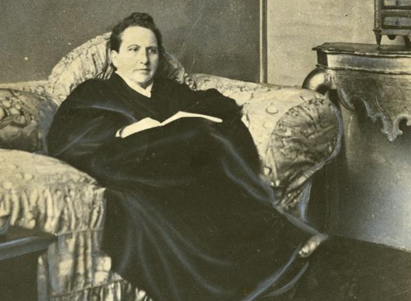 Wide World Photos, detail of Gertrude Stein sitting on a sofa in her Paris studio, with a portrait of her by Pablo Picasso, and other modern art paintings hanging on the wall behind her, May 1930. 