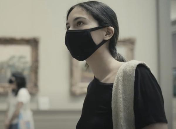 woman in mask looks at painting in the met