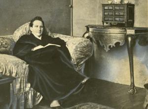 Wide World Photos, detail of Gertrude Stein sitting on a sofa in her Paris studio, with a portrait of her by Pablo Picasso, and other modern art paintings hanging on the wall behind her, May 1930. 