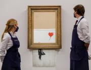 Two Sotheby's employees stand, framing the Banksy piece on auction day Oct 14, 2021