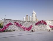 eL Seed, Declaration. Courtesy of the artist. a large installation piece in context—with city visible in the distance and children riding on bikes in front. 