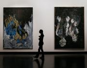 a silhouetted figure walks between two large abstract paintings