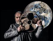 artist standing with metal fan in front of moon painting/ sculpture