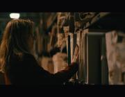 Lynda is seen in dark room, looking at shelf packed with documents. 