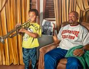 boy playing trumpet, father sits beside him holding a black and white photo