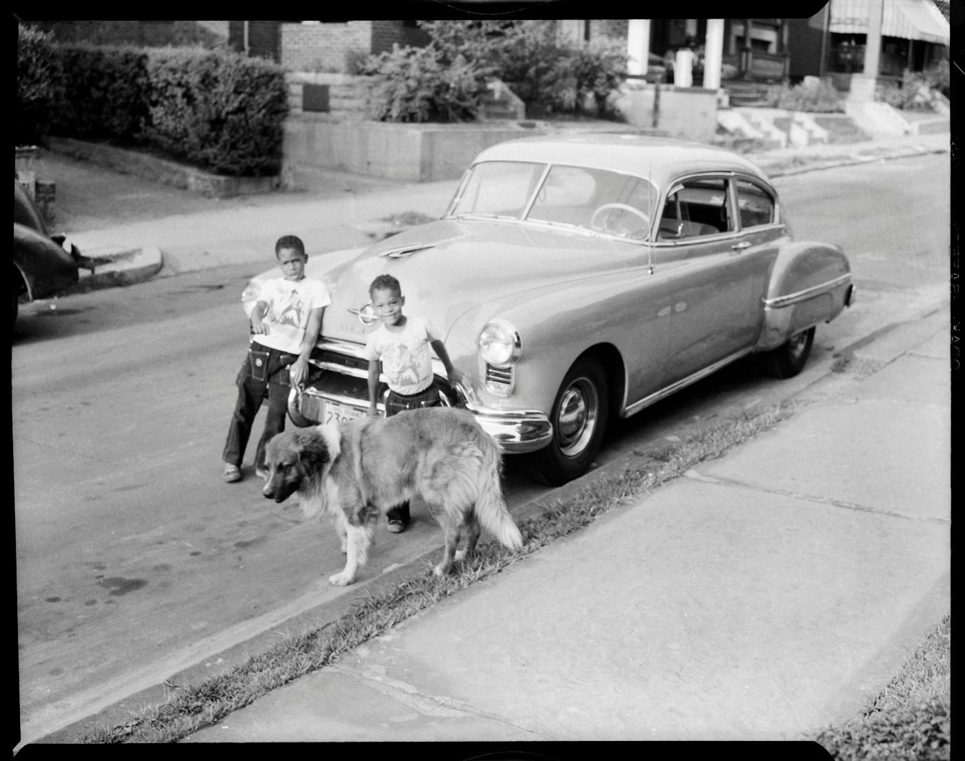 Charles “Teenie” Harris, ‘Ira Vann Harris and Lionel Harris with their dog “Joby” standing in front of parked car, on Mulford Street, Homewood,’ c. 1952