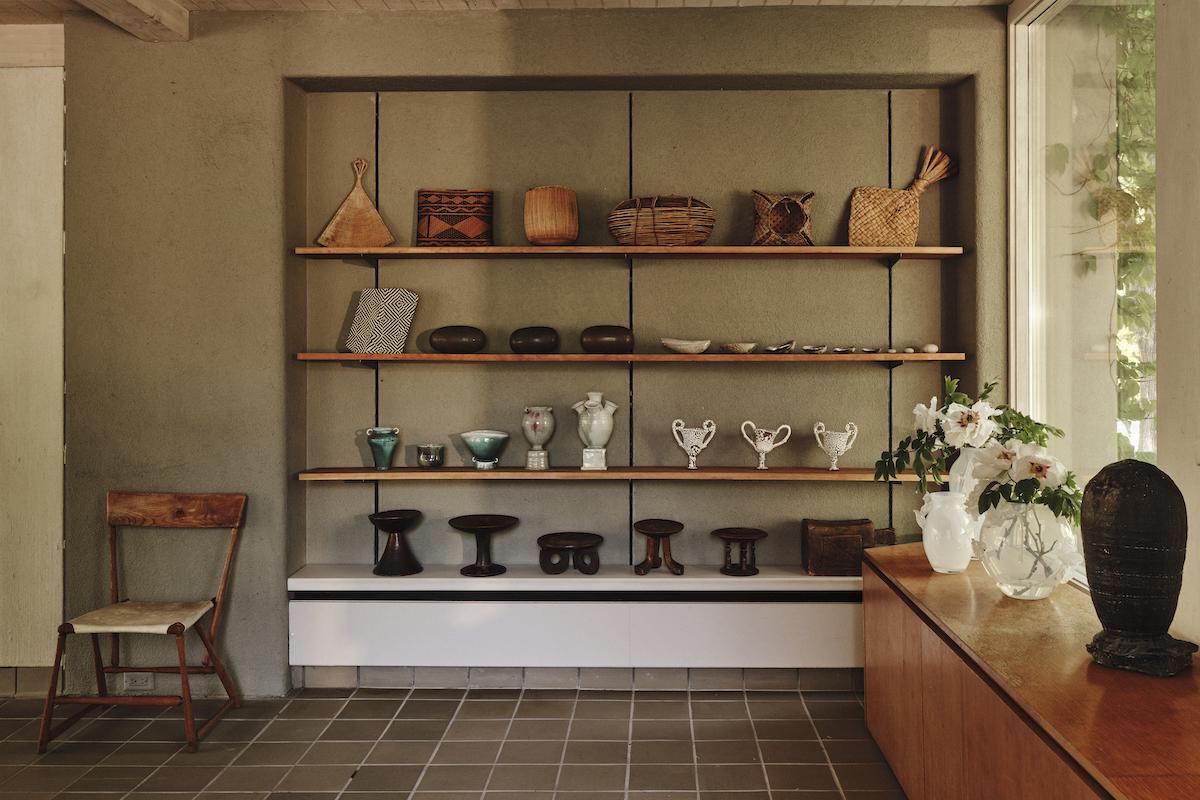 A Summer Arrangement: Object & Thing at LongHouse. LongHouse, East Hampton, New York. Photo by Adrian Gaut. Works pictured: [far left] Wharton Esherick chair from the collection of LongHouse; [shelves]; an arrangement of baskets, seed pods, shells and wooden stands from the collection of LongHouse alongside ceramics by Cody Hoyt, Frances Palmer and Raina Lee; [console]; Sophie Lou Jacobsen, Giardino Vase I, II and III (2023); Adam Silverman, Untitled (2019–19).