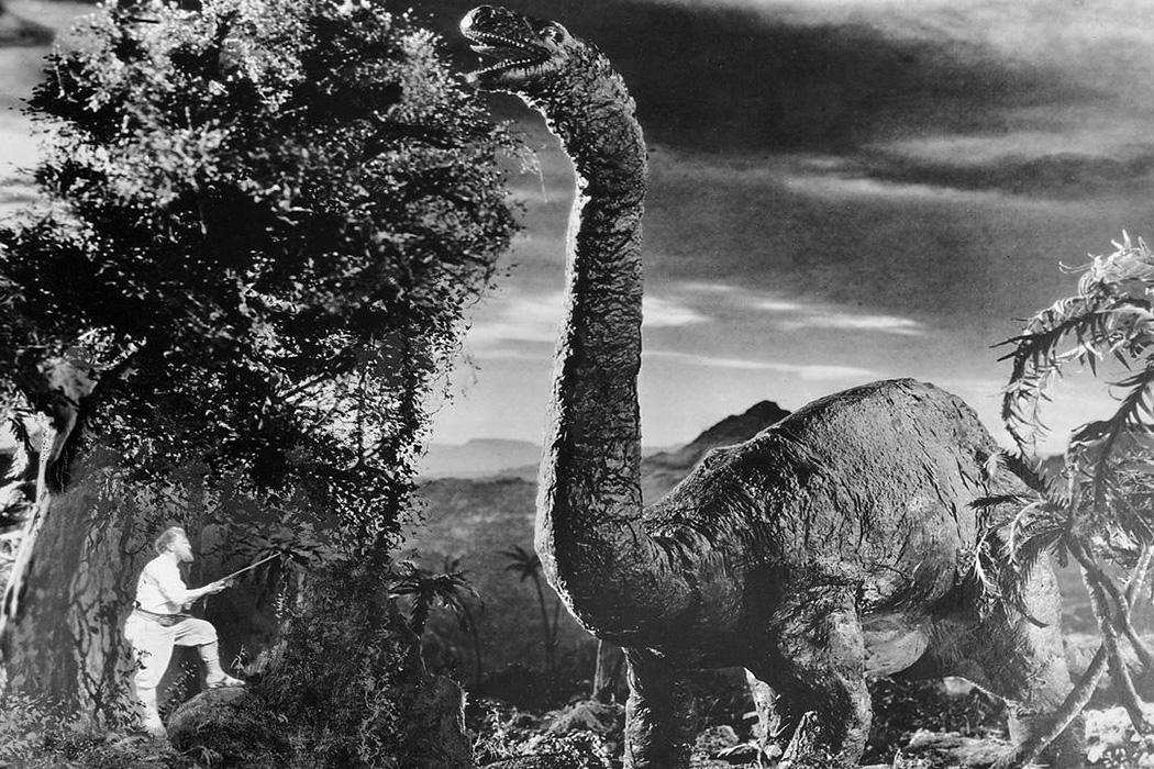 Still from The Lost World (1925) that shows a live-action actor (lower left) next to what appears to be a gigantic dinosaur (right).