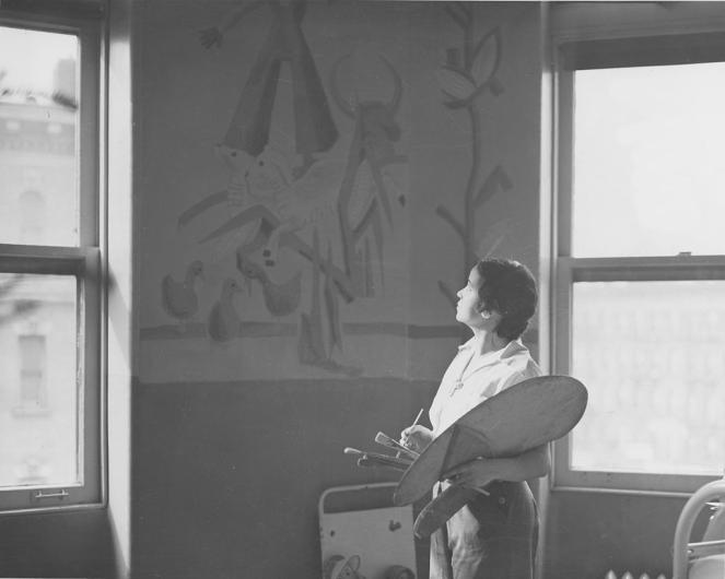 black and white photograph of elba lightfoot standing in front of an easel she's painting with palette in hand