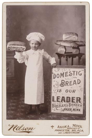 antique photograph of a child in a chef's outfit with bread