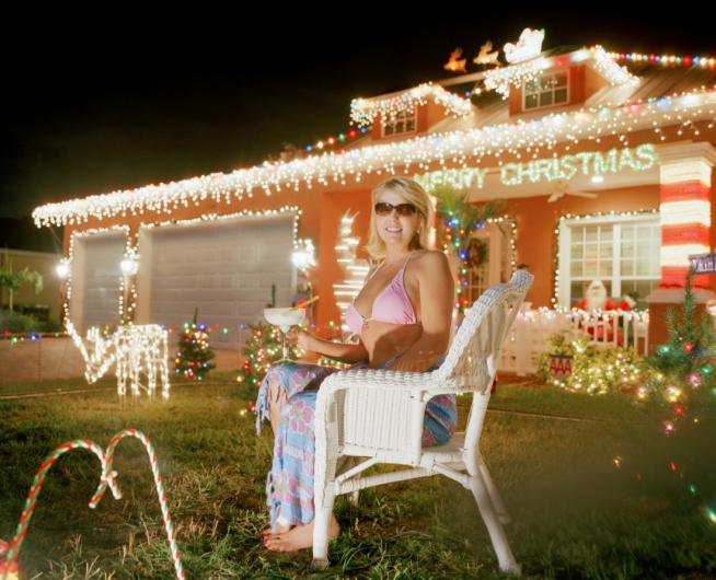 a woman in a pink bikini and sunglasses sits in a lawn chair in front of her home at night