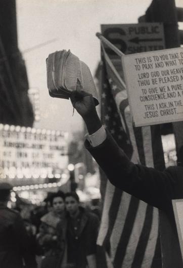 Robert Frank black and white photograph of an arm holding a stack of paper in front of a marquee