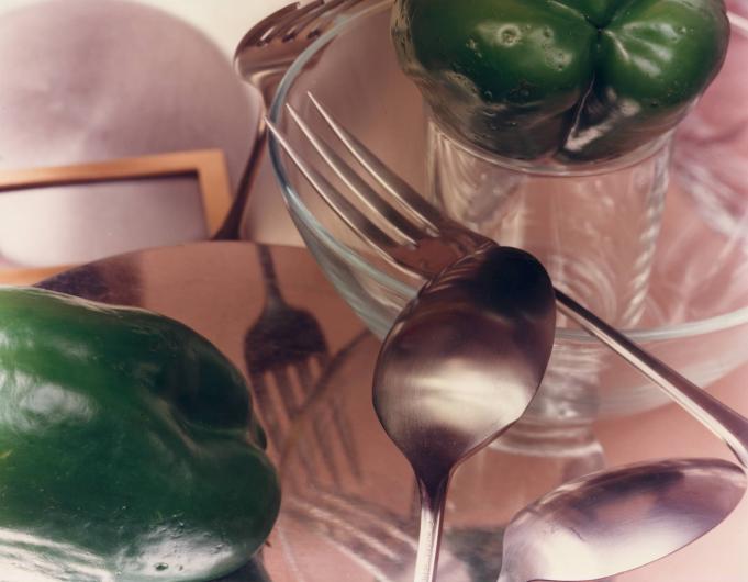 Jan Groover photograph of spoons, forks and green bell peppers on a pink tablecloth with reflected light