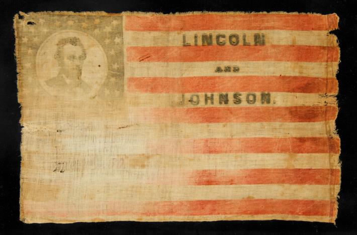 A faded old American flag with a portrait of Abraham Lincoln in the upper-left corner and the text "Lincoln and Johnson" on two white stripes