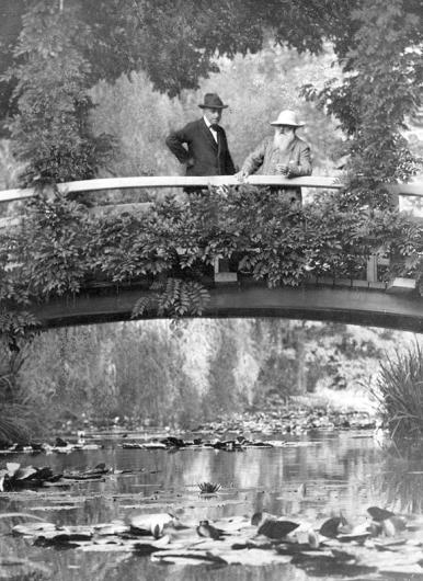 Photo of two men on a bridge over water filled with water lilies