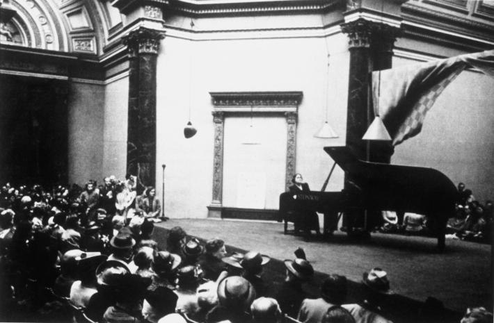black and white photograph of a woman on a stage at a grand piano in front of a crowd