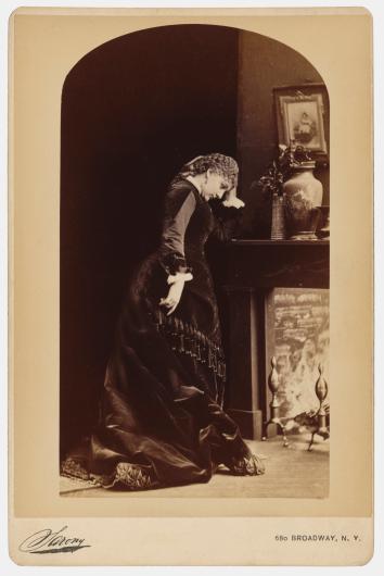 antique photo of a woman in a black dress leaning against a mantel