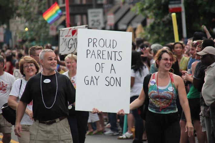 Couple holding a sign that says proud parents of a gay son